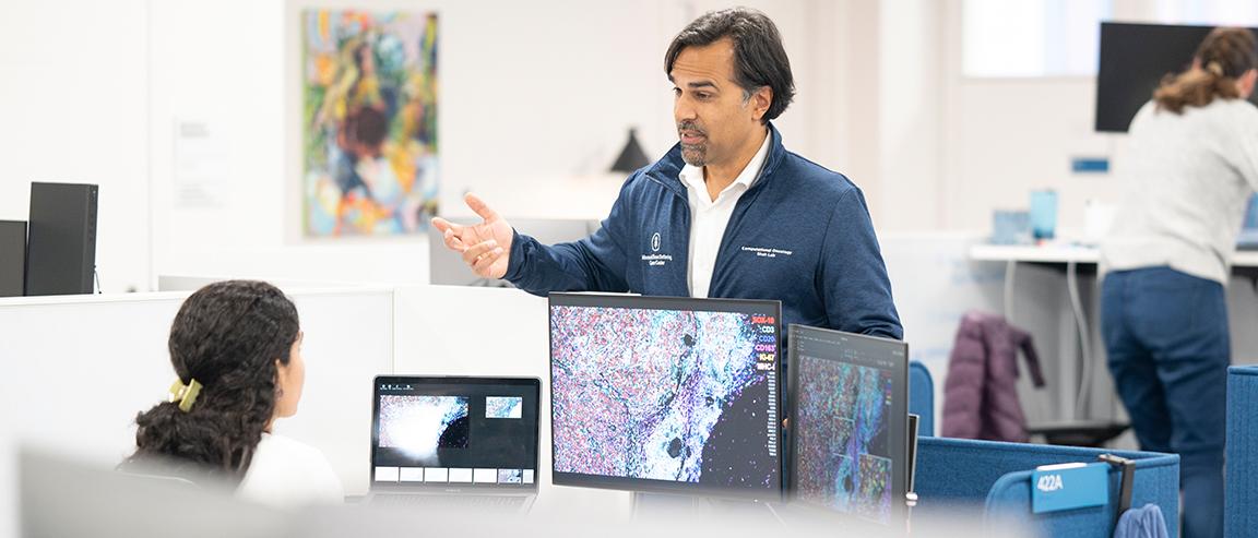 Dr. Sohrab Shah speaks to an MSK staff member who is sitting in front of a computer monitor displaying an image of cells.